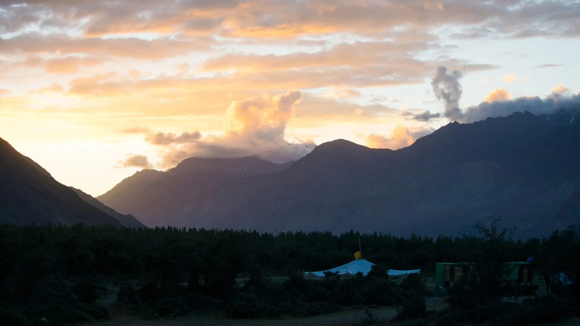 A dark valley at sunset with a plume of dust rising from the far ridge.