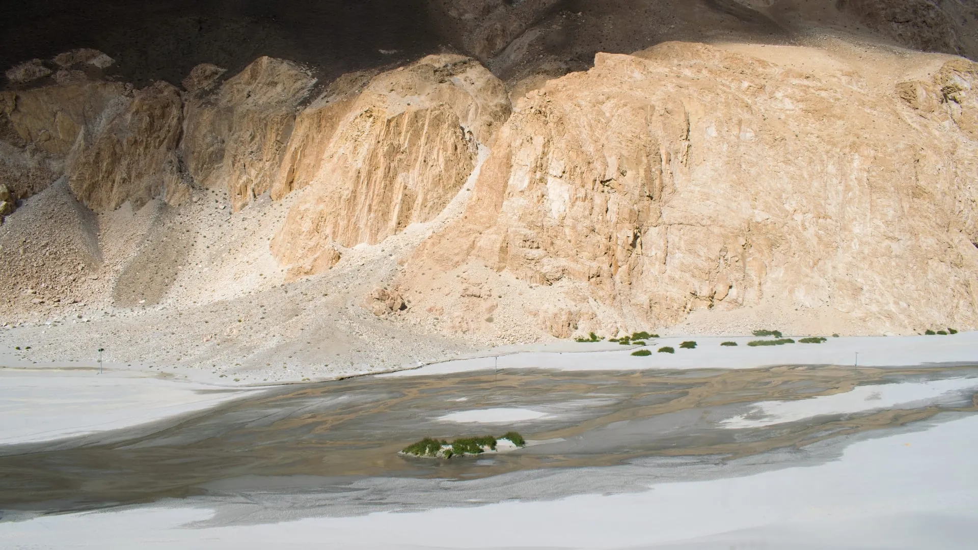 A pale eroded cliff face above a flat of grey meltwater and sand.