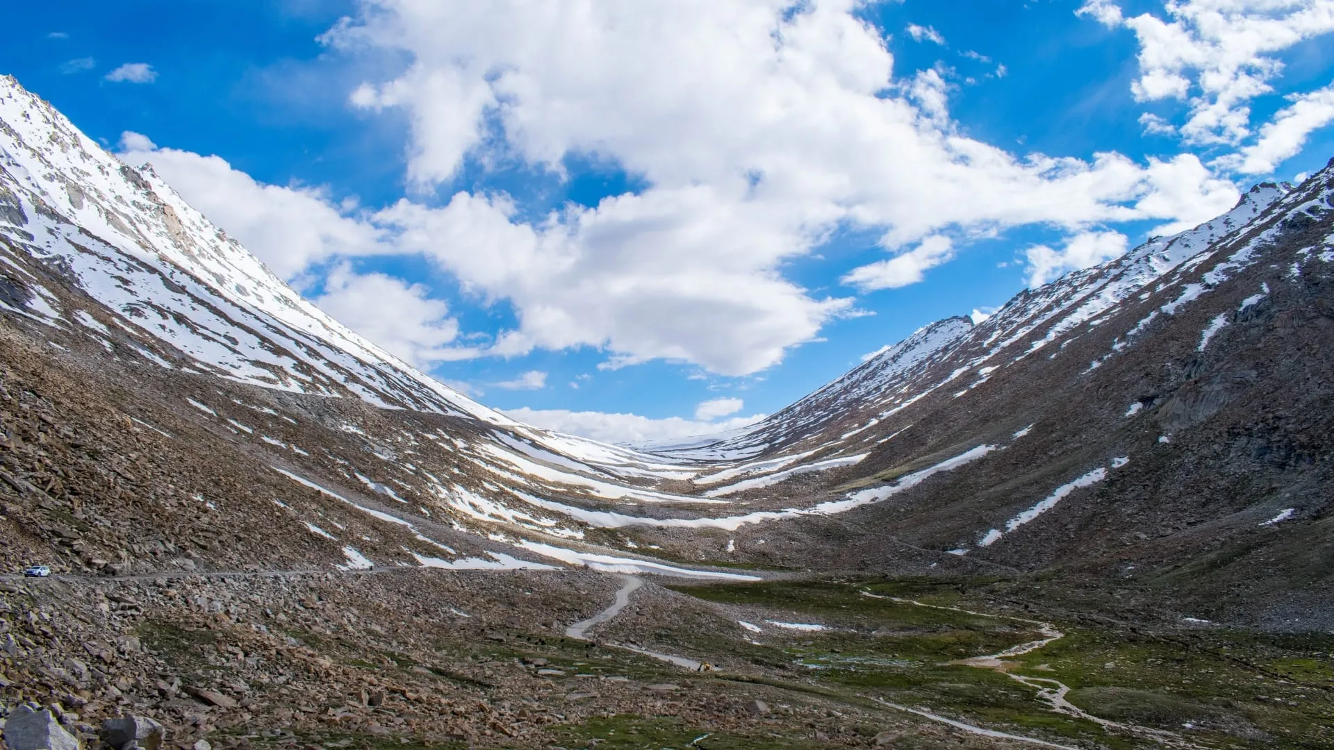 A wide glacial valley running between bare ridges, snow in the gullies, under broken cloud.