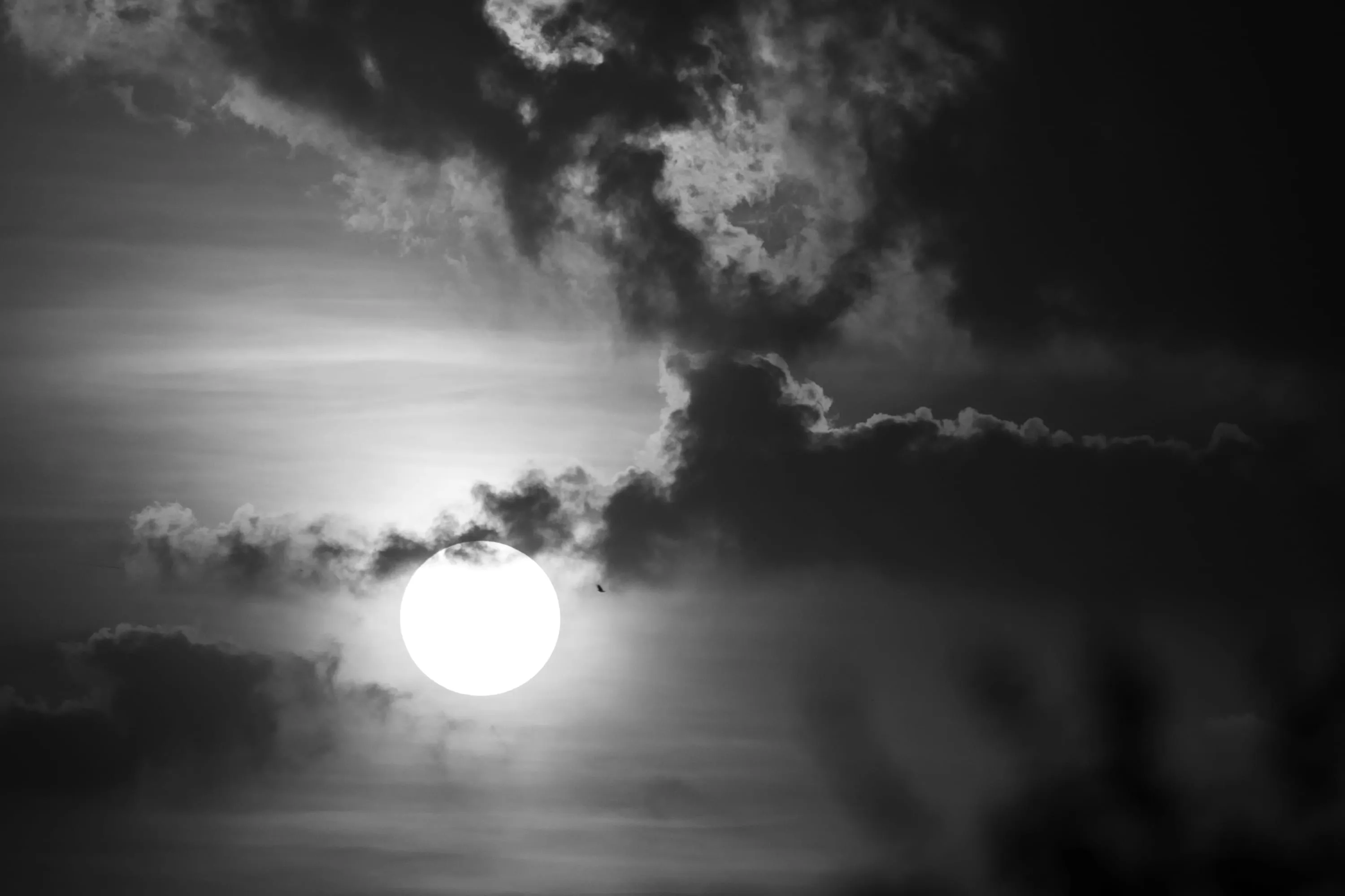 The moon burning through broken cloud, rendered in monochrome.
