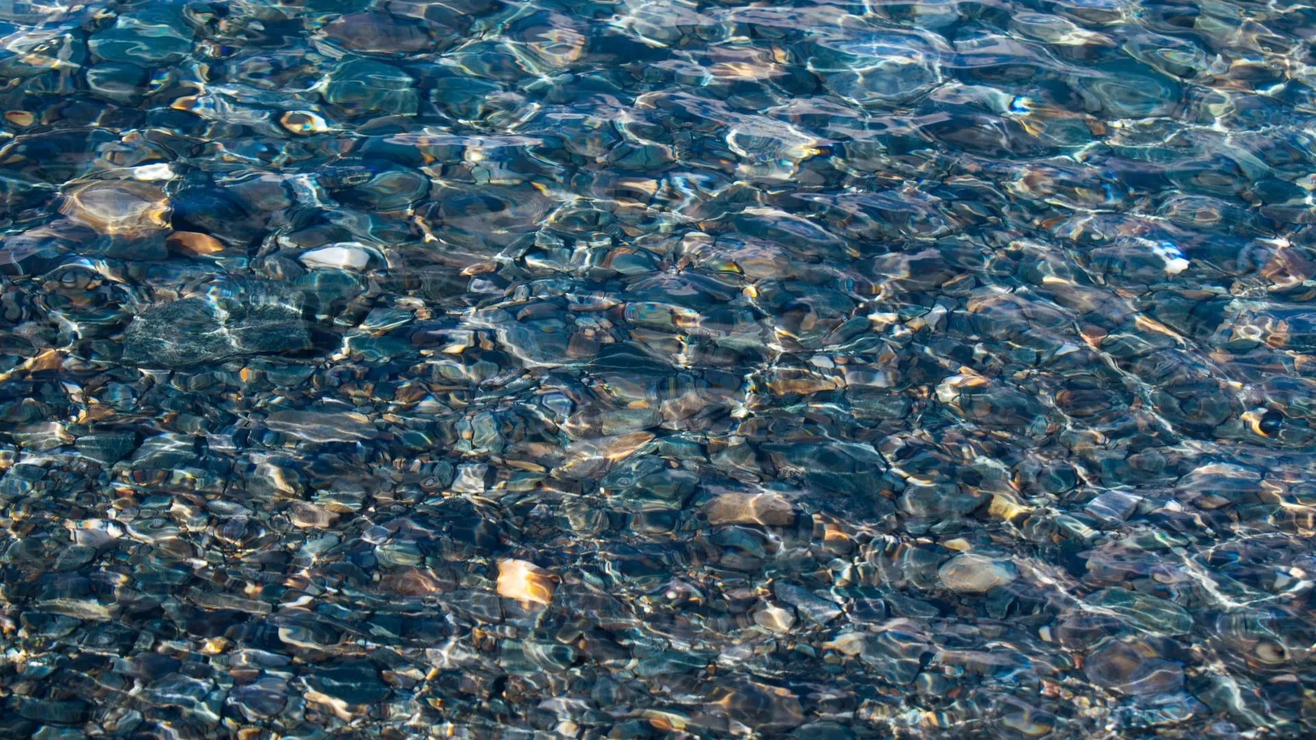 Coloured pebbles seen through a few centimetres of clear, moving water.