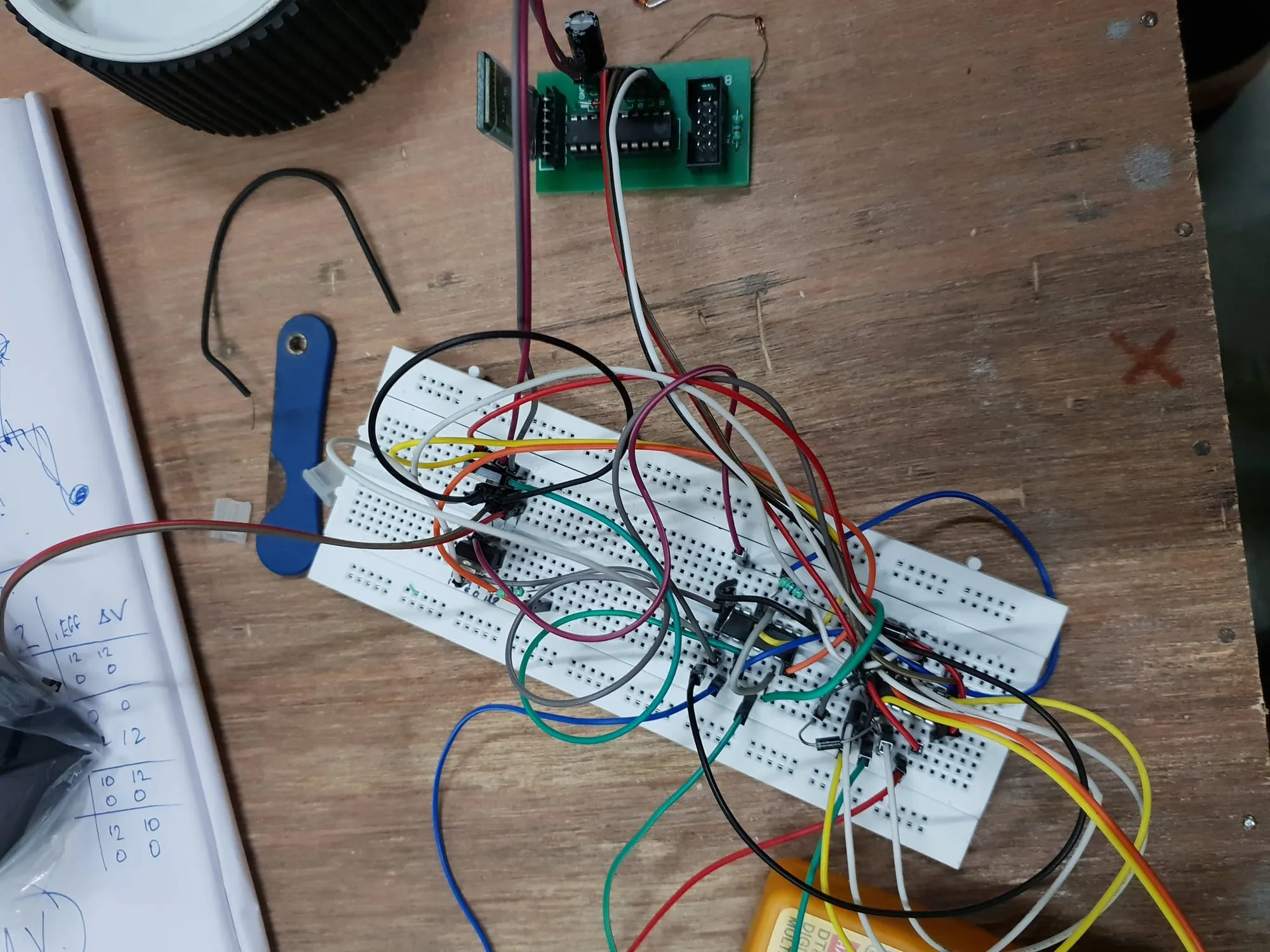 A wooden workbench with two breadboards under a tangle of jumper wires, the finished green driver board above them, and a hand-written table of readings on the notepad alongside.