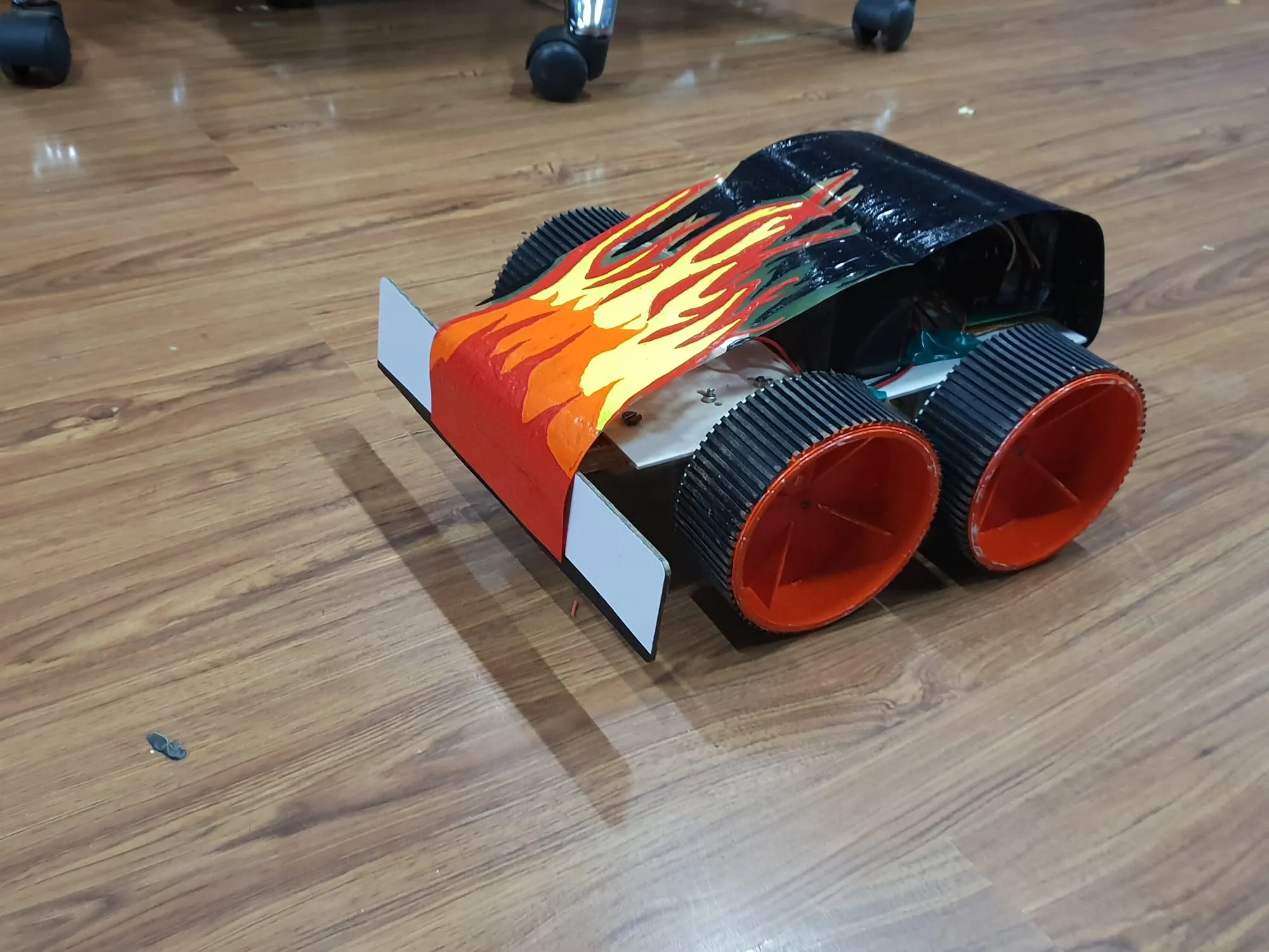 The same bot seen from behind and above, the front wing catching the light and the electronics visible in the gap under the shell.