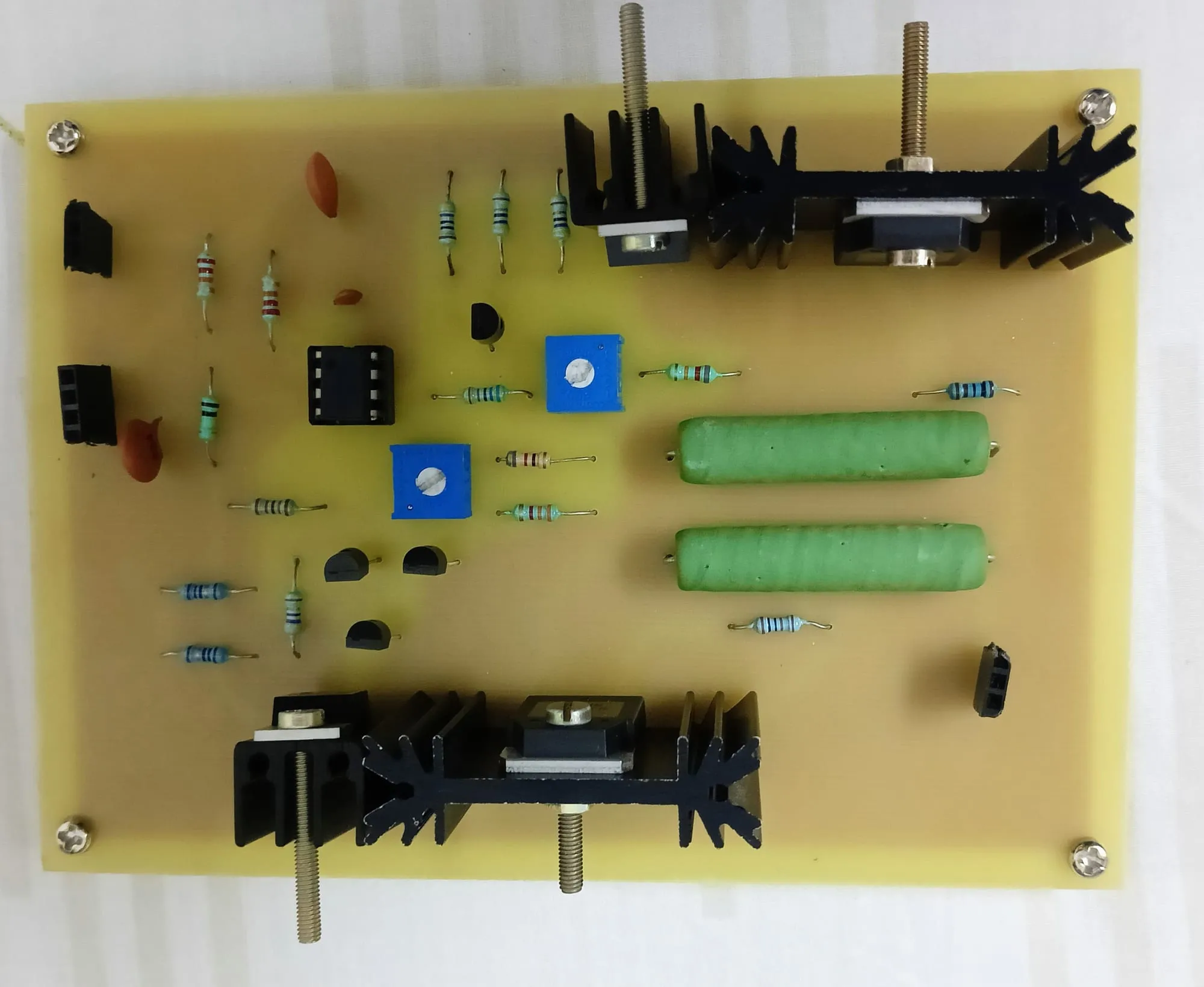 A populated single-sided PCB: black heatsinks along two edges, green wirewound resistors, blue trimpots and through-hole components on a yellow board.