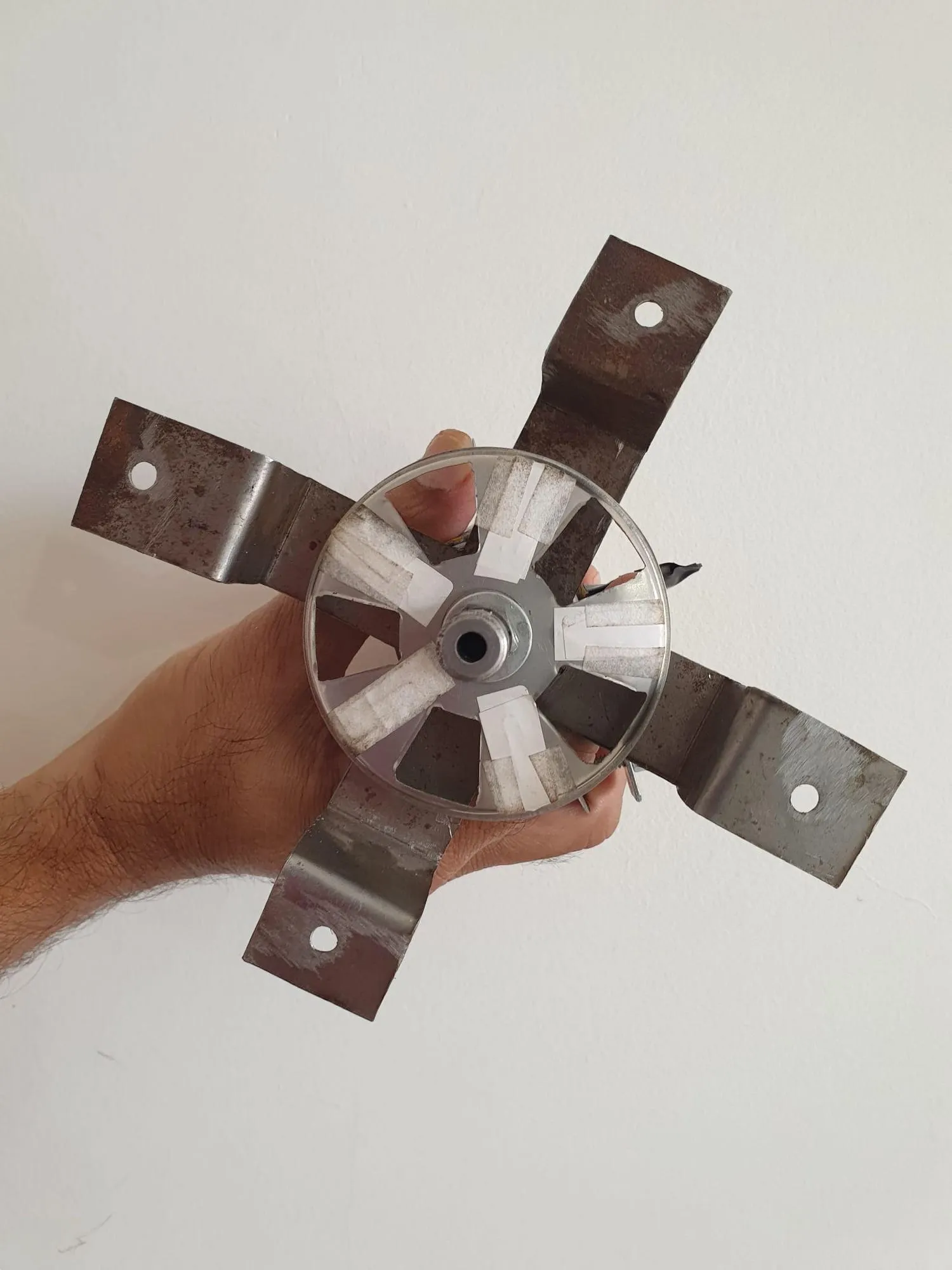 A slotted aluminium disc with four flat metal arms bolted around it, held in one hand.